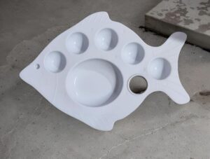 White fish-shaped plastic mold with multiple round wells and a large central depression, resting on a concrete floor.