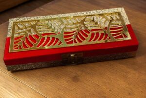 Red velvet jewelry box with an ornate gold lattice lid resting on a wooden surface, with a small latch in front.