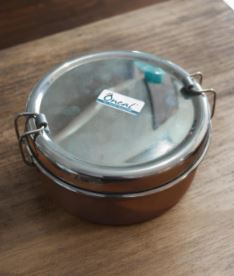 Round stainless steel insulated lunch pot with a clasp lid on a wooden table surface.