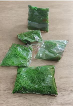 Clear plastic bags filled with bright green powder arranged on a light wooden surface.