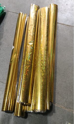 Pile of gold metallic wrapping paper rolls stacked on a concrete floor outside.