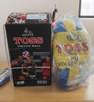 Box of Toss volleyball set beside a plastic bag of Toss yellow and blue volleyballs on a wooden table (box shows players and logo).