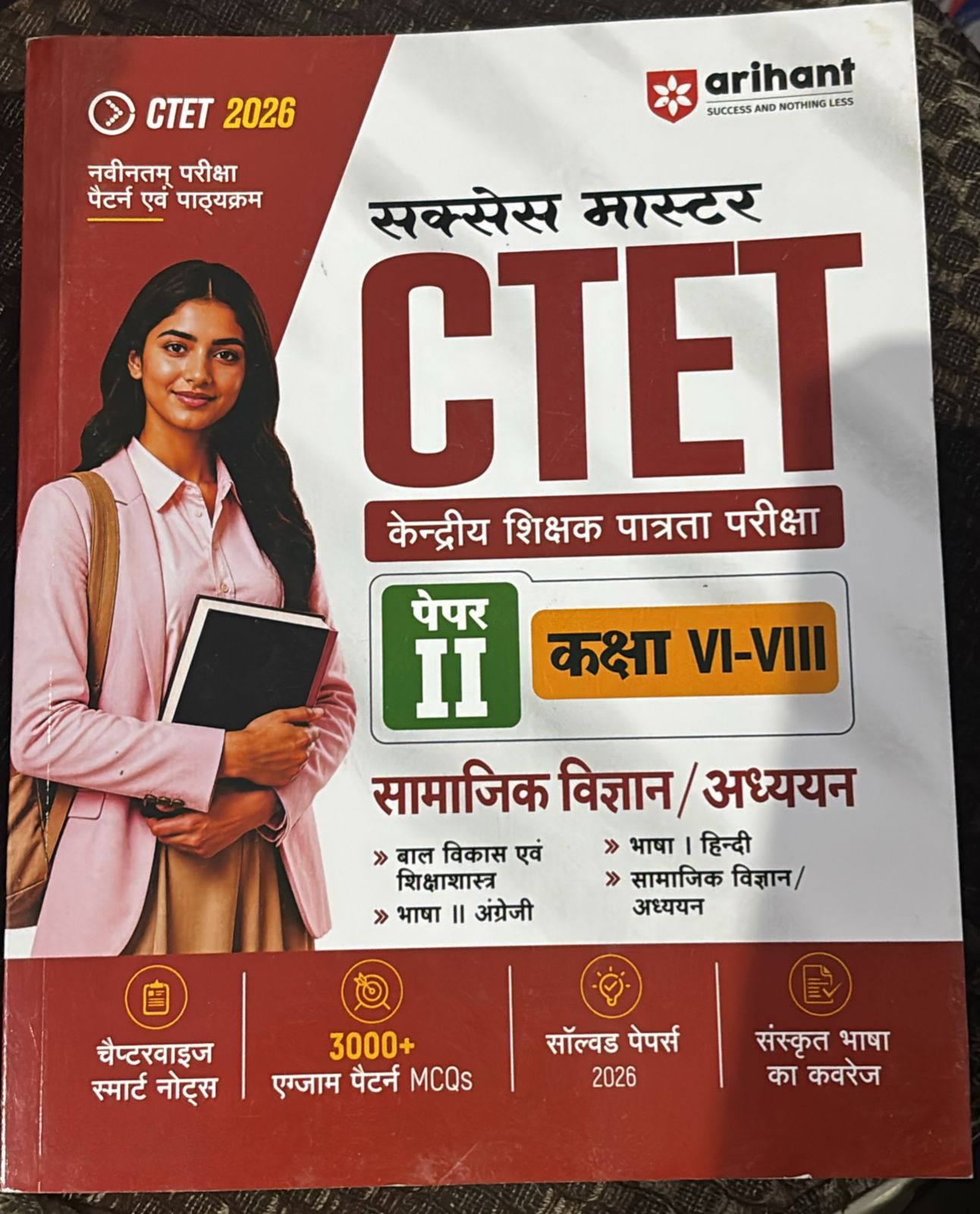 Book cover for CET 2026 exam preparation featuring a smiling woman in a pink blazer holding notebooks; large 'CET' title, Hindi subtitle, and Arihant logo.