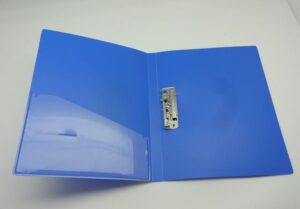 Open blue binder laid flat with metal ring mechanism in the center and a clear plastic pocket on the left cover.