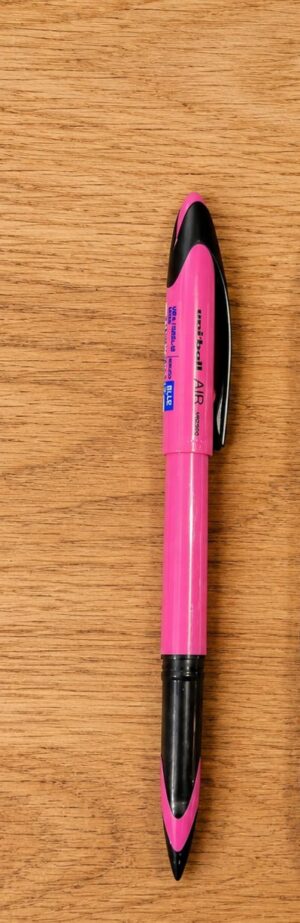 Pink and black retractable pen lying on a wooden surface.