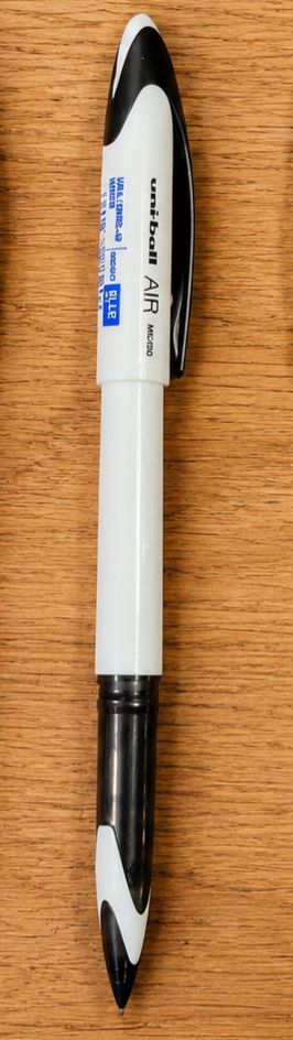 White and black uni-ball AIR marker pen lying on a wood surface, white body with black end caps and a blue label visible.