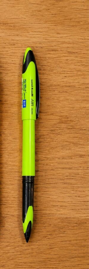 Fluorescent yellow highlighter with black accents lying on a wooden surface, cap and tip visible.