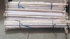 Bundle of long white cylindrical items wrapped in plastic and secured with blue straps on a concrete floor.