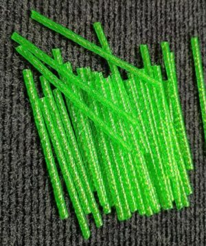 Pile of bright green, flat plastic sticks scattered on a dark textured surface (carpet)