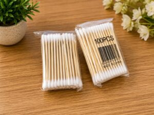 Two packs of cotton swabs on a wooden table, each in clear plastic wrapping with a 100 PCS label on the right pack.