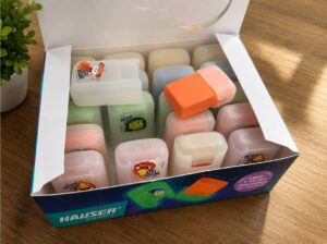 Box of colorful erasers still in packaging, open on a wooden table with a small plant nearby