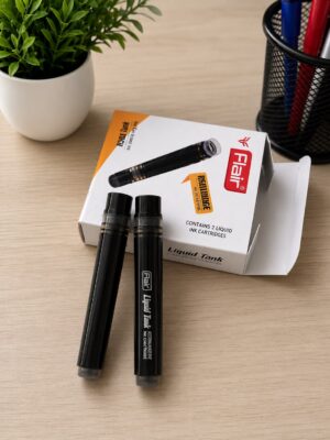 Two black Flair liquid ink pens on a desk with a white box labeled ‘Flair Liquid Tank’ and a plant in the background, a pen holder to the right.