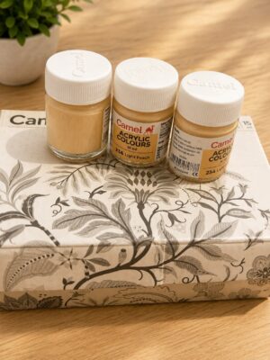 Three Camel acrylic colour jars (15 ml) in light peach/beige on a decorative patterned box atop a wooden table, white lids visible with Camel branding.