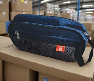 Blue nylon fanny pack with a zippered pocket resting on a cardboard box in a warehouse setting.