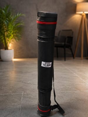 Tall black cylindrical case with red bands stands upright on a gray tiled floor in a living room, with a plant and a lamp in the background.