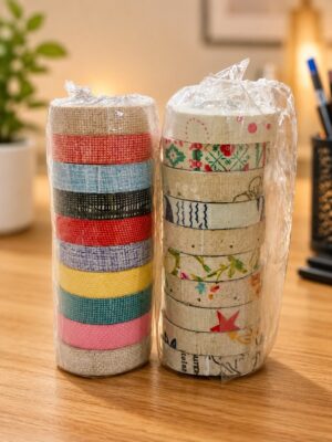 Two wrapped spools of decorative washi tape stacked on a wooden desk, left with solid colors and right with patterns/prints.