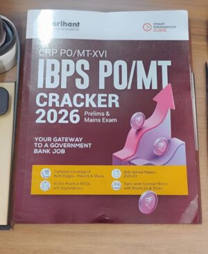 Study guide book titled 'IBPS PO/MT Cracker 2026' on desk, with pink upward arrow graphic and yellow info strip indicating features like practice MCQs and solved papers (front cover).