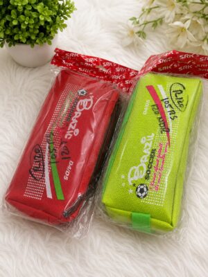 Two colorful rectangular pencil cases in clear plastic packaging on a white fluffy surface—red and neon green with soccer ball graphics.