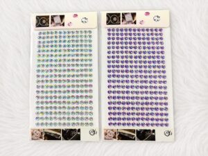 Two sheets of small, colorful rhinestone stickers arranged in a grid on a white surface with decorative header and footer cards, left iridescent and right purple.