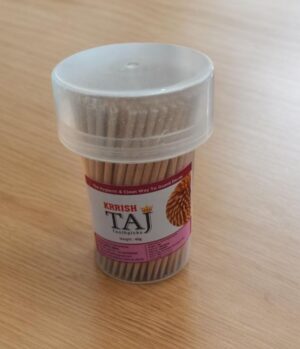 Container of toothpicks (Krrish Taj) with a clear lid, placed on a wooden table, pink label visible on the side.