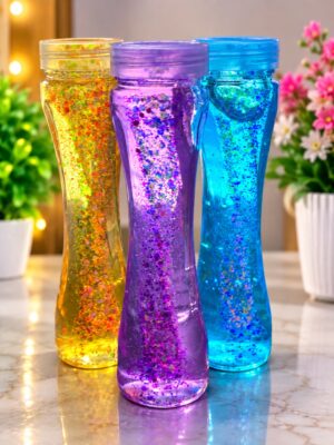 Three glitter-filled plastic bottles in yellow, purple, and blue with curved shapes on a marble countertop.