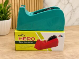 Teal plastic tape dispenser resting on its yellow Unity Hero tape dispenser box on a wooden desk.