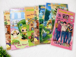 Assorted kids' sticker books in plastic sleeves laid out on a white surface with colorful cartoon covers.