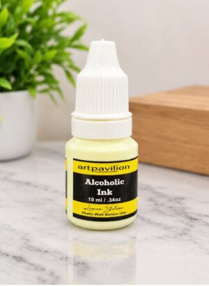 Bottle of ArtPavilion Lemon Yellow Alcohol Ink (10 ml) on a marble surface with a plant in the background.