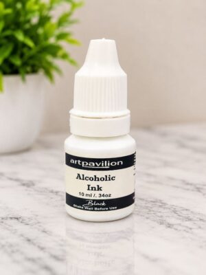 Small white bottle labeled 'ArtPavilion Alcohol Ink Black' (10 ml) on a marble surface, with a blurred green plant in the background.