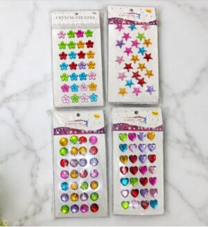 Four packs of adhesive craft stickers on a white marble surface: flowers, stars, round gems, and heart gems.